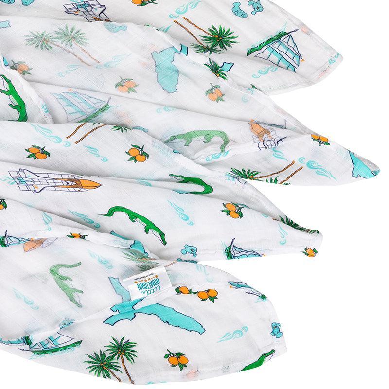 Florida-themed baby muslin swaddle blanket with colorful illustrations of palm trees, flamingos, and oranges.