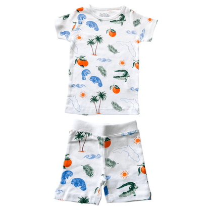 Child's pajamas with Florida-themed illustrations, including oranges, flamingos, and palm trees on a white background.