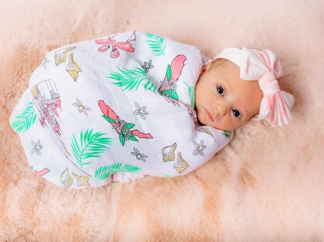 Floral muslin swaddle blanket and burp cloth set with pink, yellow, and green flowers on a white background.