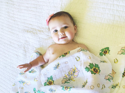 Floral-themed baby gift set with a muslin swaddle blanket and burp cloth/bib combo, featuring pink and green flowers.