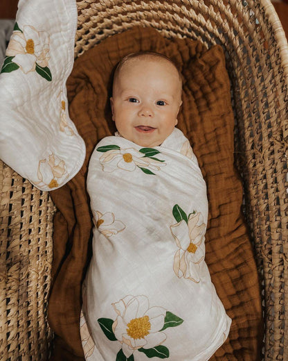 Southern Magnolia baby muslin swaddle blanket and burp cloth set with delicate floral design on a white background.