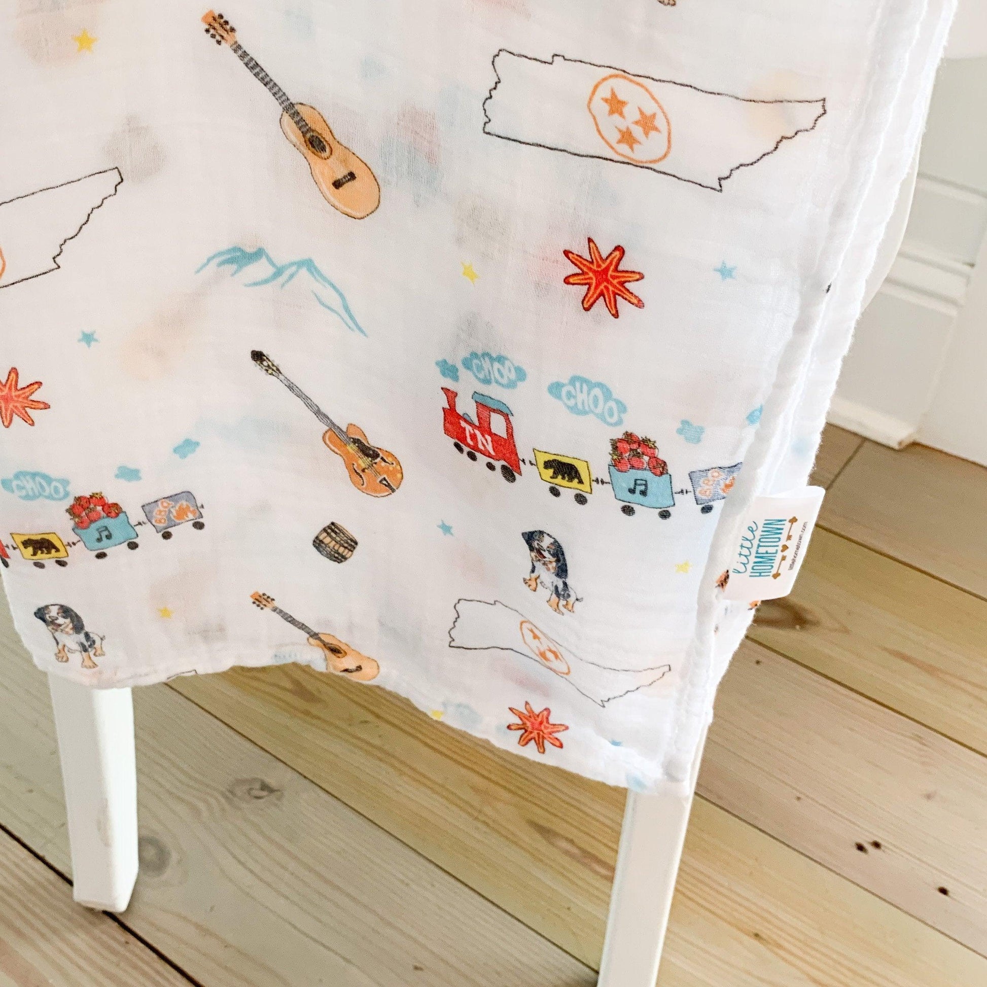 Tennessee-themed baby gift set with muslin swaddle blanket and burp cloth, featuring state icons and landmarks.