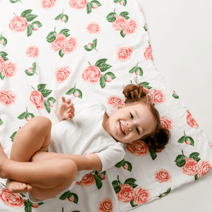 Soft pink muslin swaddle blanket and matching burp cloth with delicate white camellia flower pattern.