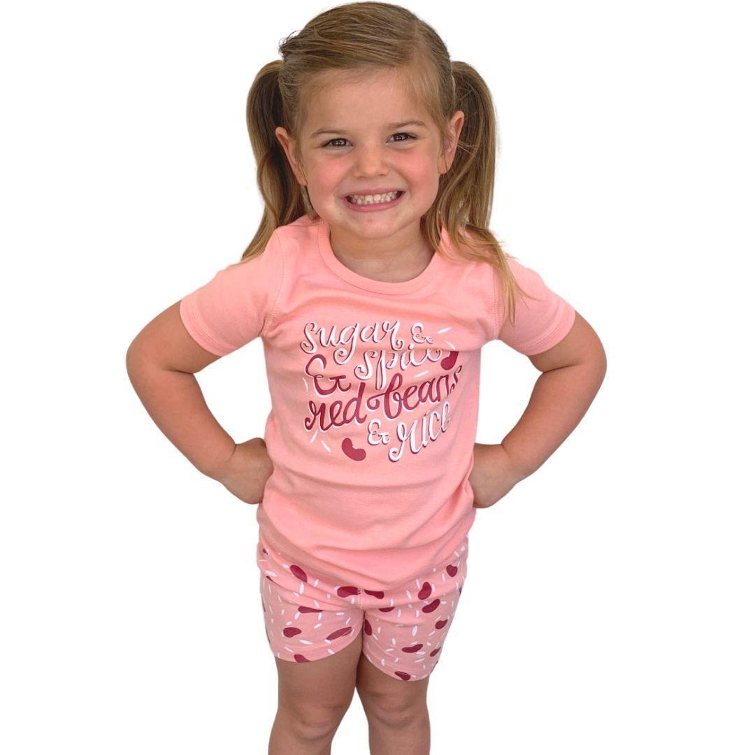 Toddler wearing red pajamas with white rice and beans print, smiling and sitting on a white background.