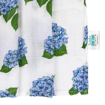 Soft muslin baby swaddle blanket with delicate hydrangea print in pastel blues and greens, folded neatly.