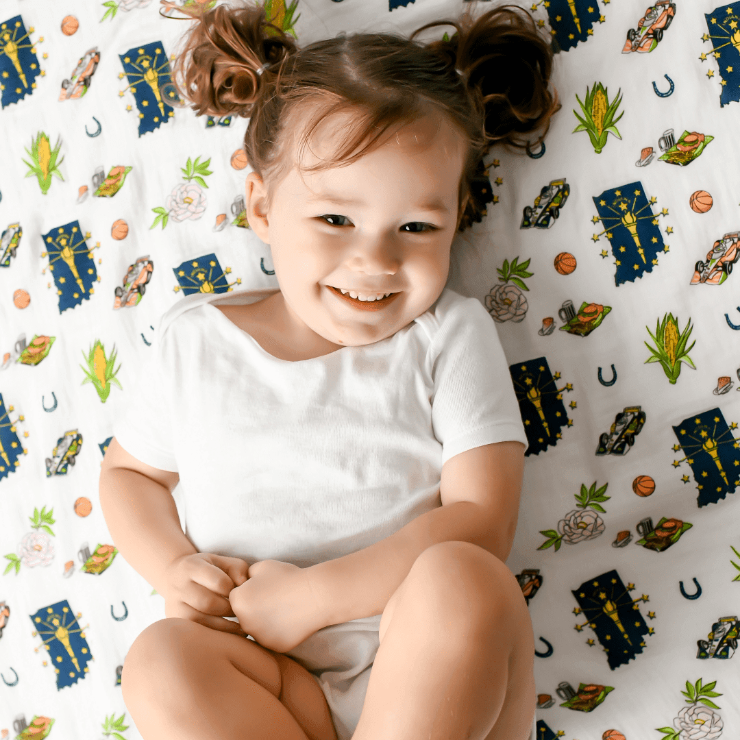 Indiana-themed baby muslin swaddle blanket with state icons like race cars, basketballs, and corn, on a white background.