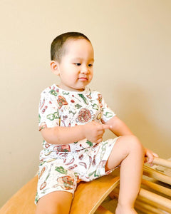 Toddler wearing colorful Jambalaya-themed pajamas with shrimp, sausage, and rice illustrations, smiling joyfully.
