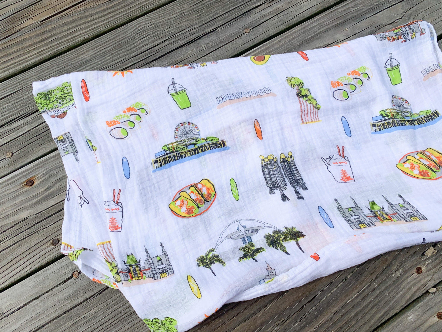 White muslin swaddle blanket with "Los Angeles" text and iconic city landmarks in soft pastel colors.