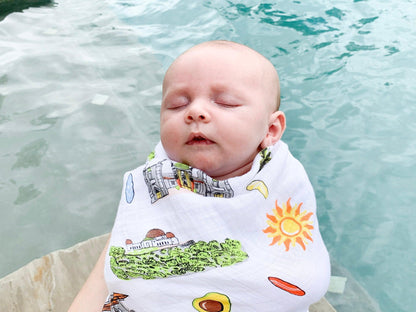 Los Angeles-themed baby muslin swaddle blanket with iconic landmarks and palm trees, in soft pastel colors.