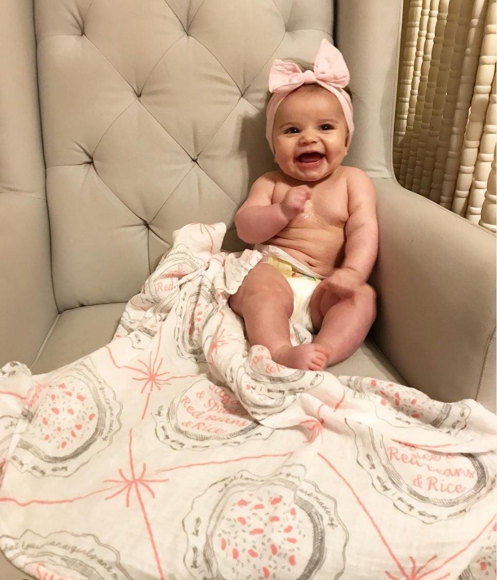 Louisiana-themed baby girl muslin swaddle blanket with pink and white design, featuring state icons and "Louisiana" text.