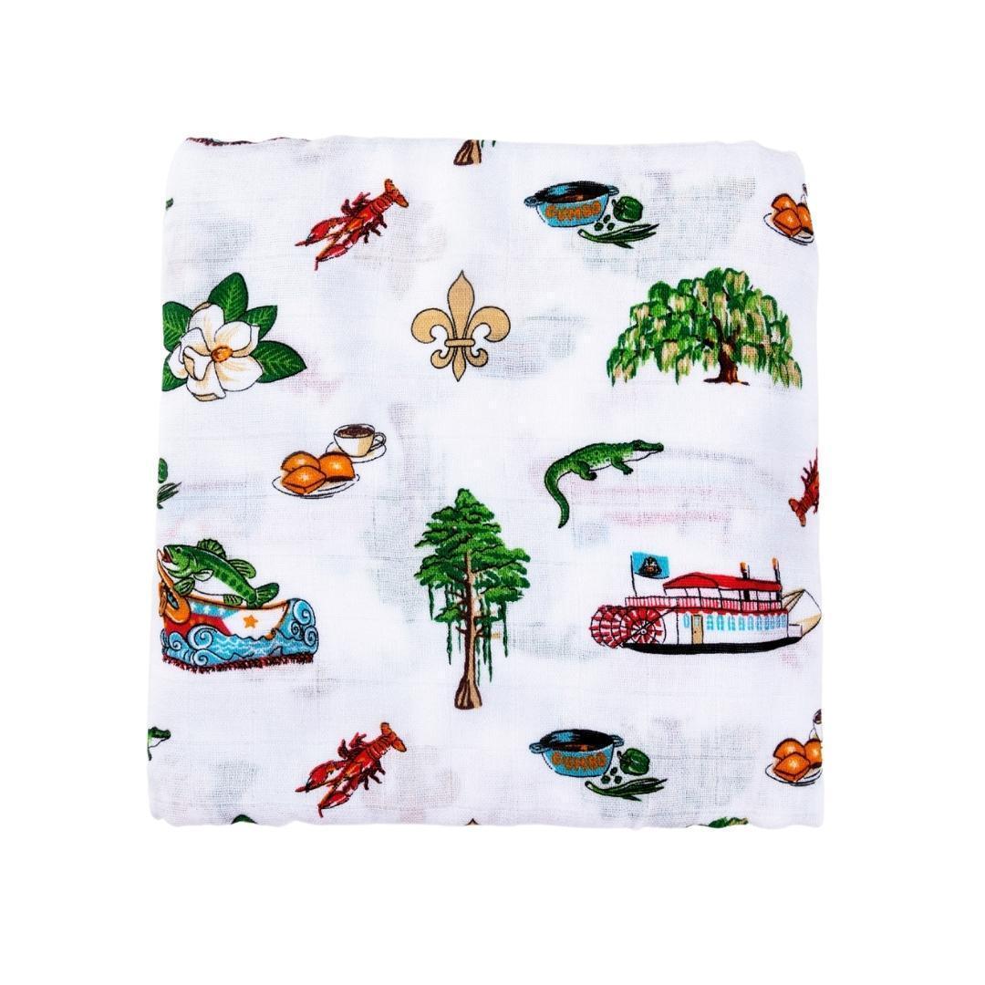 White muslin swaddle blanket with colorful Louisiana-themed illustrations, including pelicans, crawfish, and magnolias.