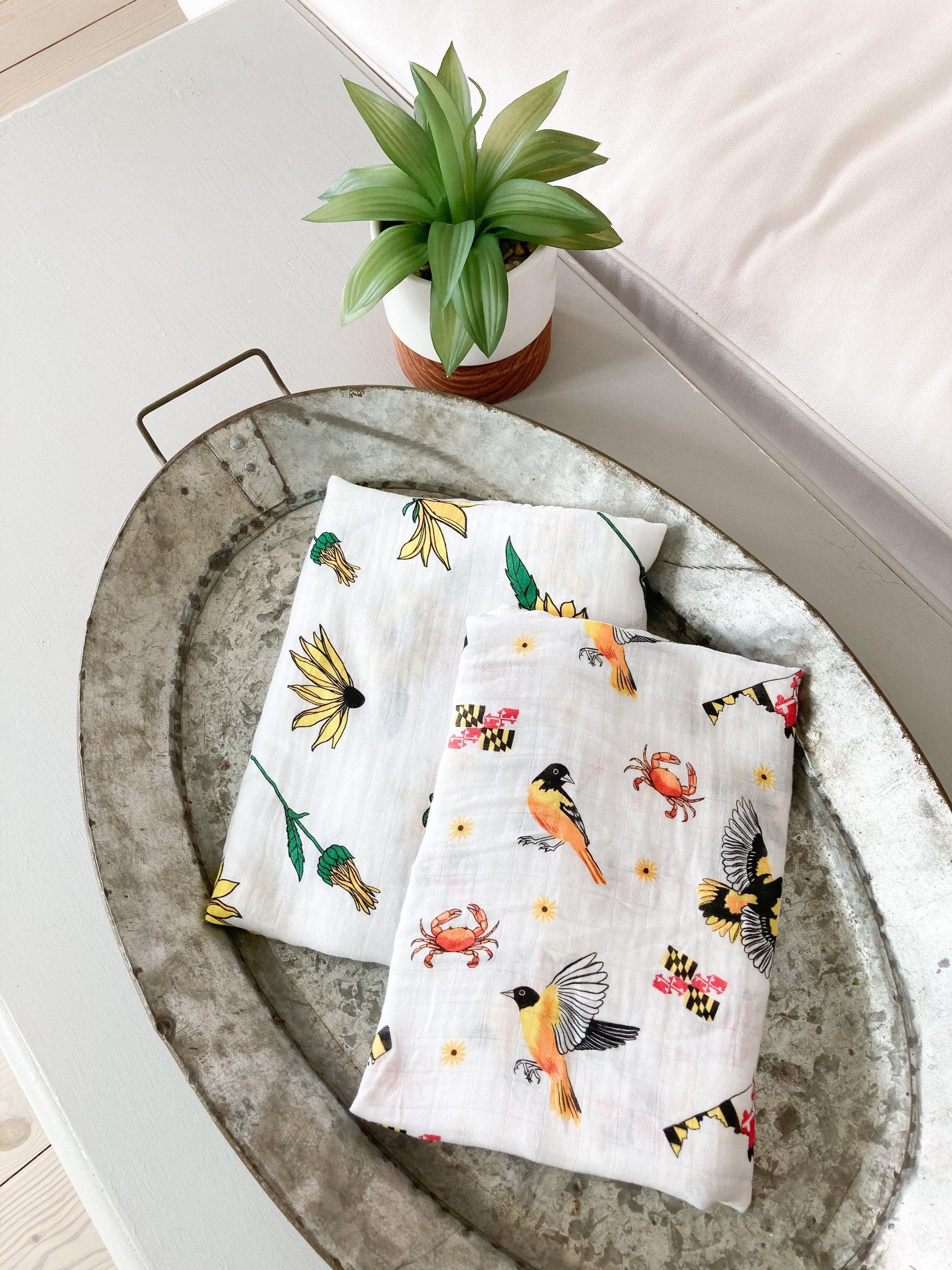 White muslin baby swaddle blanket with Maryland-themed illustrations, including crabs, flags, and lighthouses.
