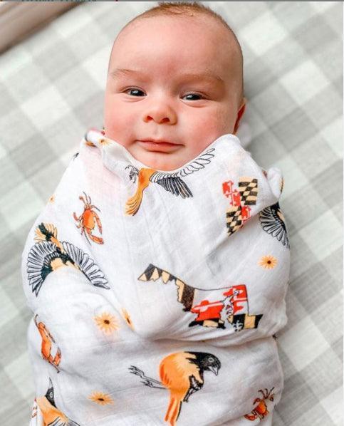 White muslin baby swaddle blanket with Maryland-themed illustrations, including crabs, lighthouses, and state symbols.