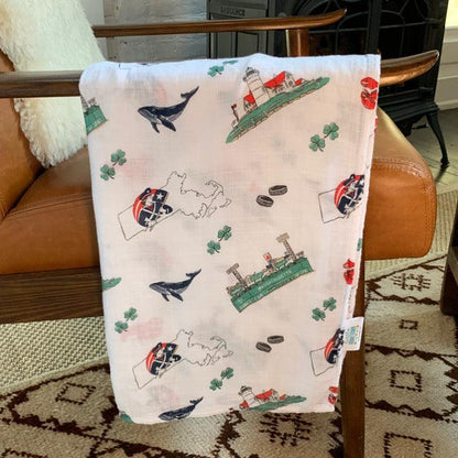 Massachusetts-themed baby muslin swaddle blanket with state icons and landmarks in soft pastel colors.