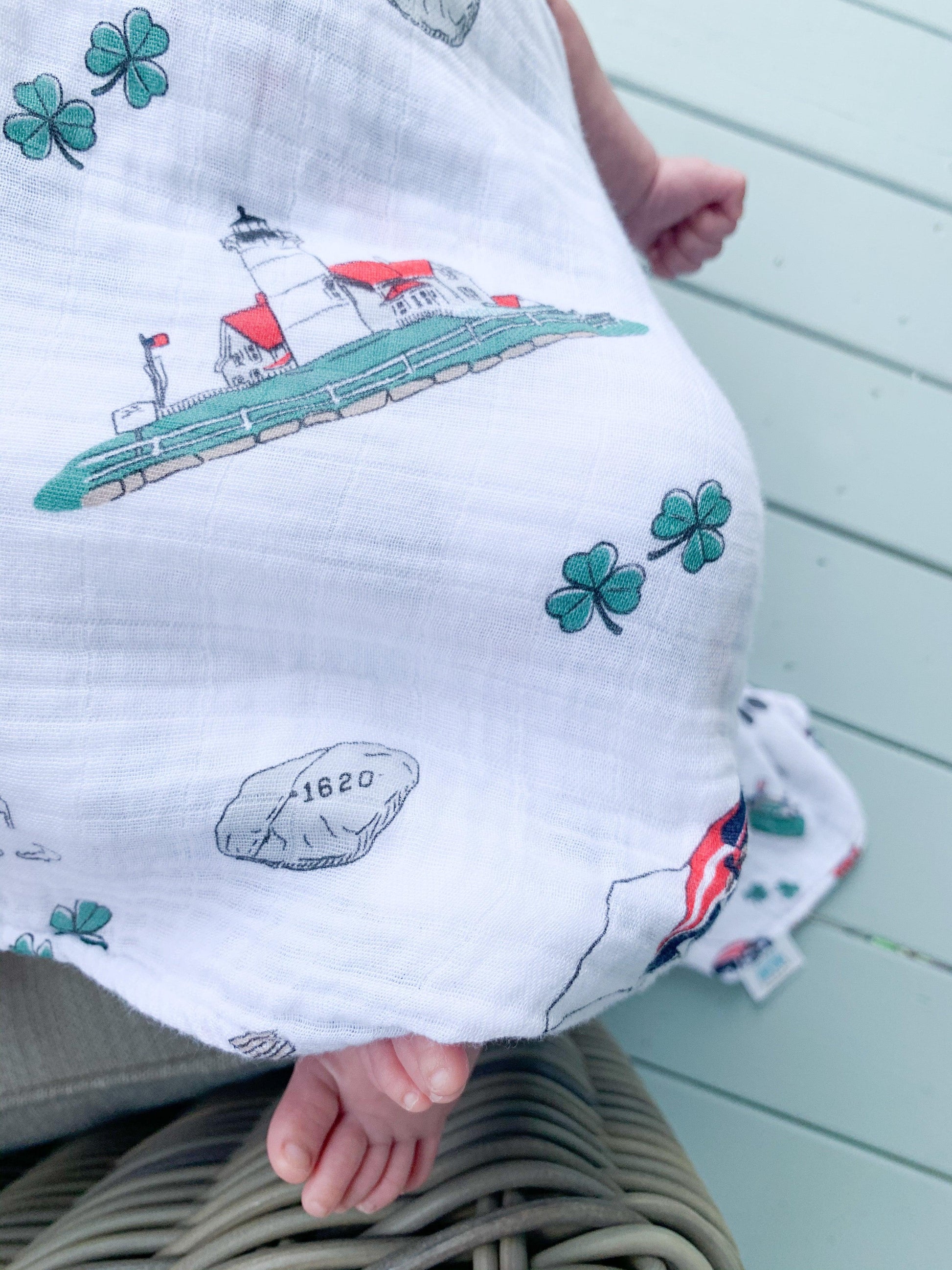 Massachusetts-themed baby muslin swaddle blanket with state icons and landmarks in soft pastel colors.