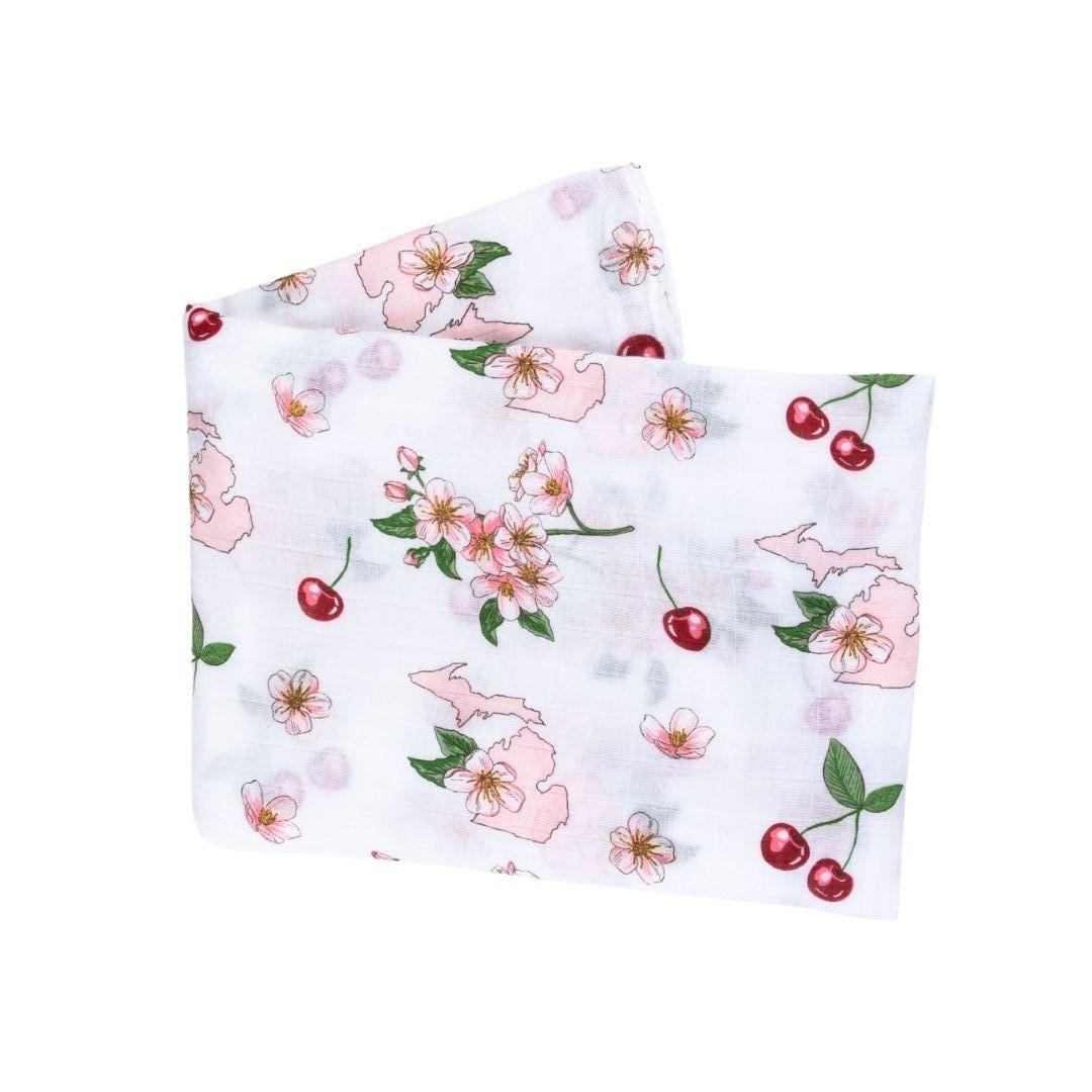 White muslin swaddle blanket with colorful floral patterns and "Michigan" text, draped on a soft surface.