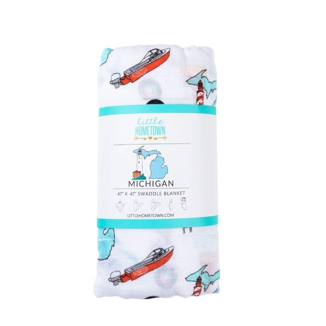 White muslin swaddle blanket with Michigan-themed illustrations, including landmarks, animals, and state symbols.
