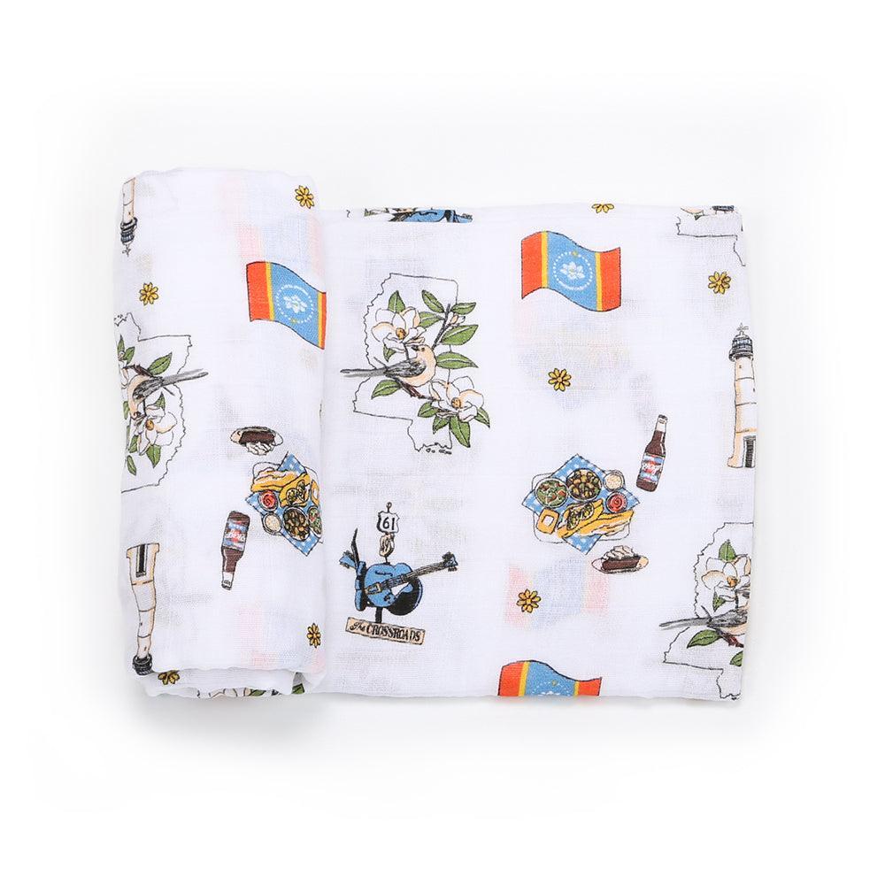 White muslin swaddle blanket with a colorful map of Mississippi, featuring landmarks and playful illustrations.