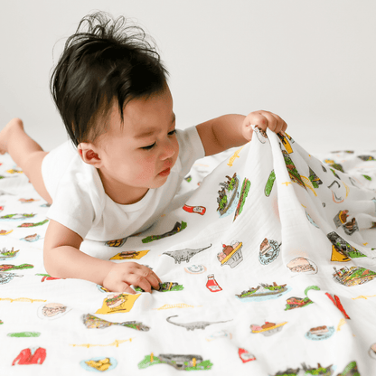 White muslin baby swaddle blanket with Pittsburgh landmarks and icons in black and yellow illustrations.