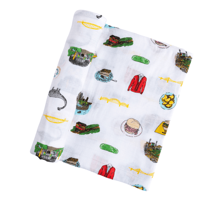 White muslin baby swaddle blanket with Pittsburgh landmarks and icons, including bridges, sports logos, and buildings.