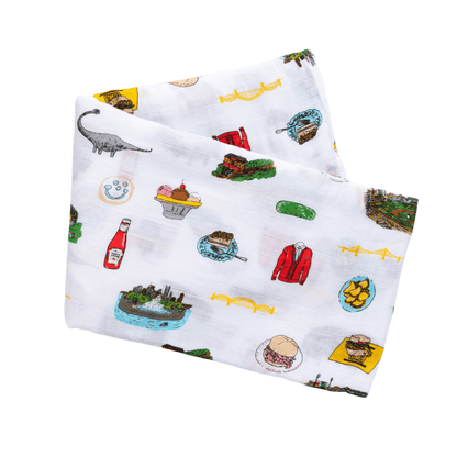 White muslin baby swaddle blanket with Pittsburgh landmarks and icons in black and yellow illustrations.