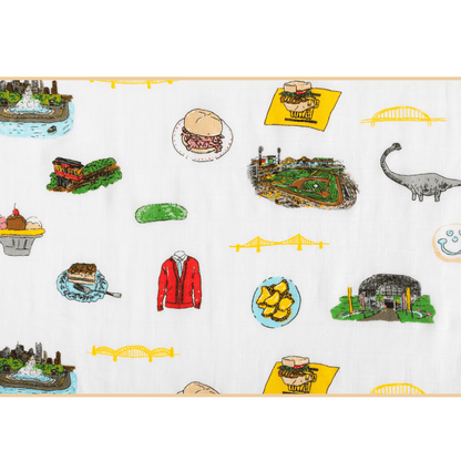 White muslin baby swaddle blanket with Pittsburgh landmarks, including bridges, skyline, and sports icons.