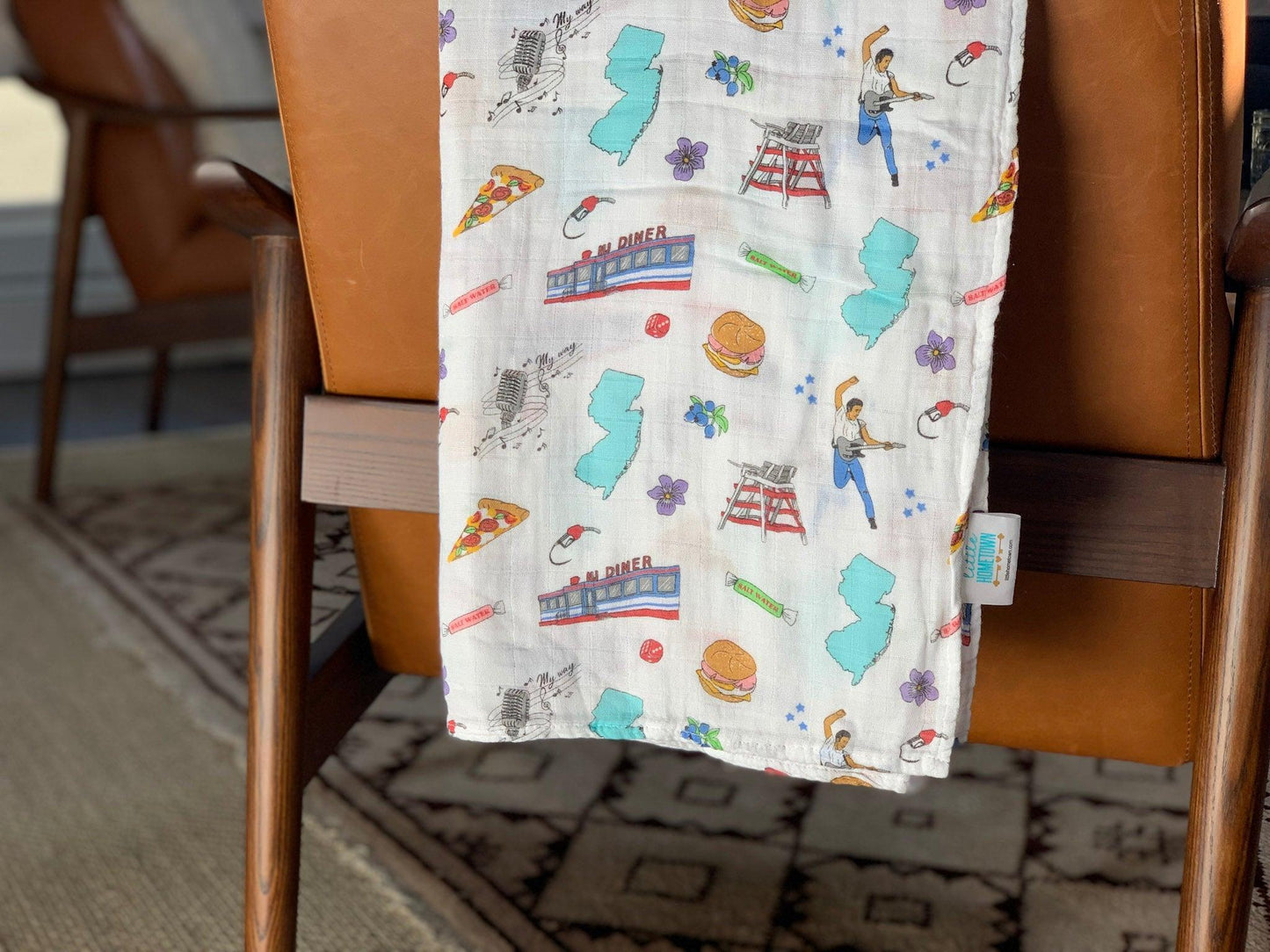 White muslin swaddle blanket with a colorful New Jersey map, featuring landmarks, animals, and state symbols.