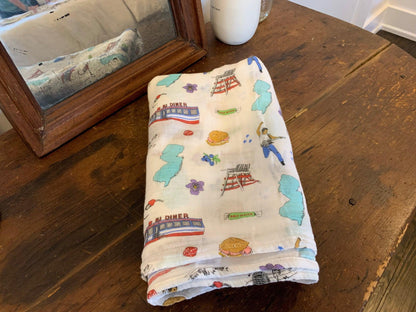 New Jersey-themed baby muslin swaddle blanket with state icons and landmarks in soft pastel colors.