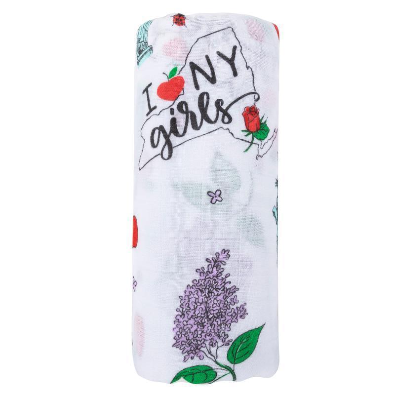 White muslin swaddle blanket with pink and blue New York-themed illustrations, including the Statue of Liberty and taxis.