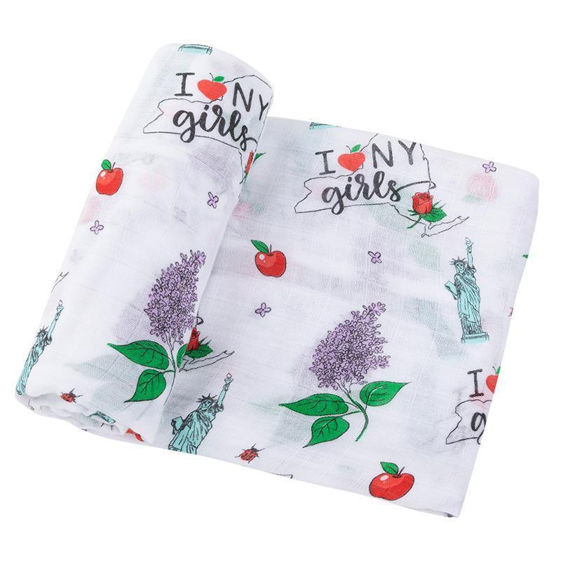 New York-themed baby girl muslin swaddle blanket with iconic landmarks in pastel colors on a white background.