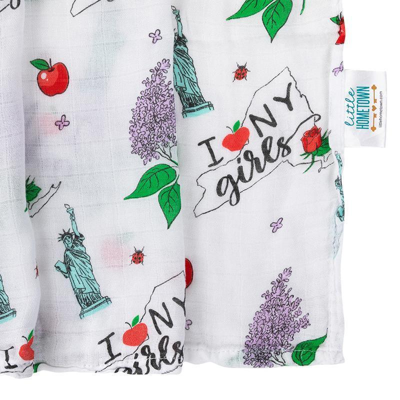 Baby girl swaddled in a white muslin blanket with New York-themed illustrations, including the Statue of Liberty and taxis.