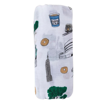 White muslin swaddle blanket featuring colorful illustrations of New York City landmarks and icons.