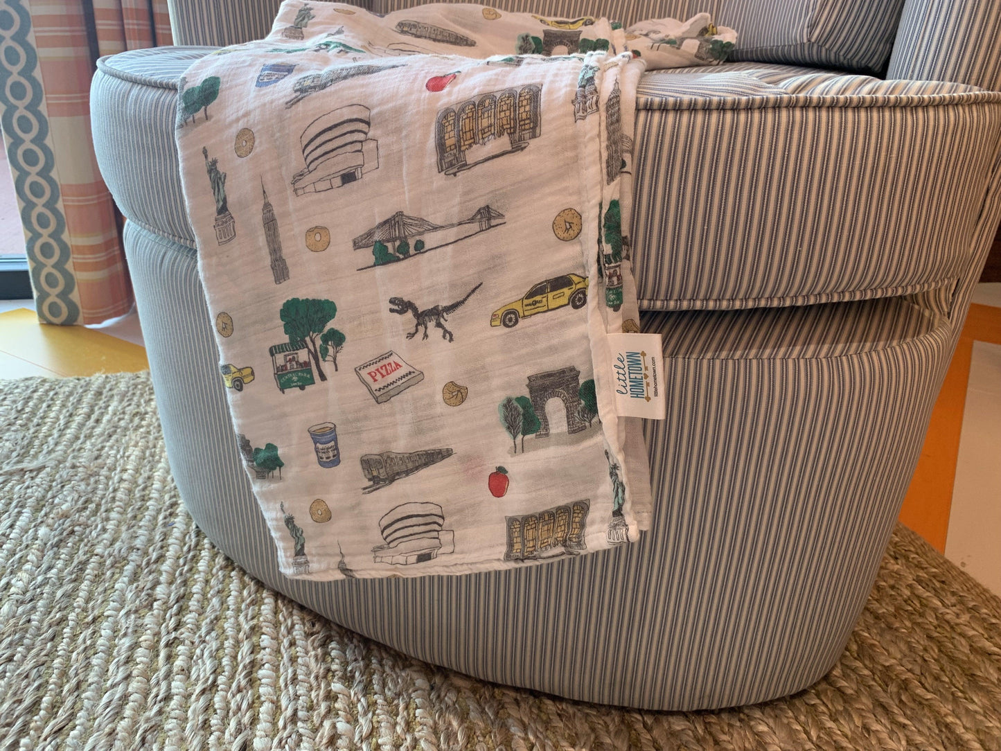 White muslin swaddle blanket with colorful New York City icons, including the Statue of Liberty, taxis, and skyscrapers.