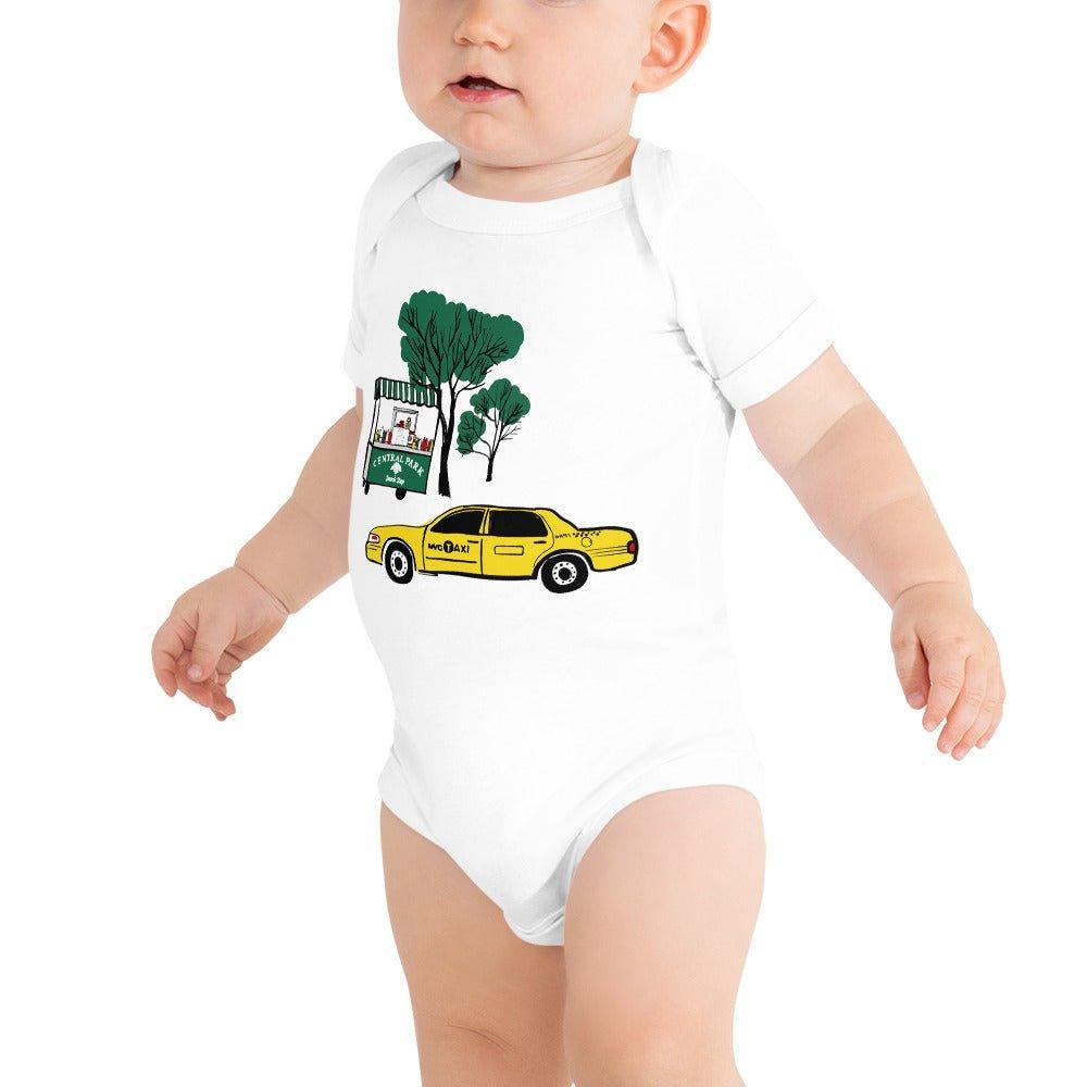 Baby wearing a onesie with "Central Park" text on a food cart next to a green tree, and a NYC yellow taxi driving in front of it