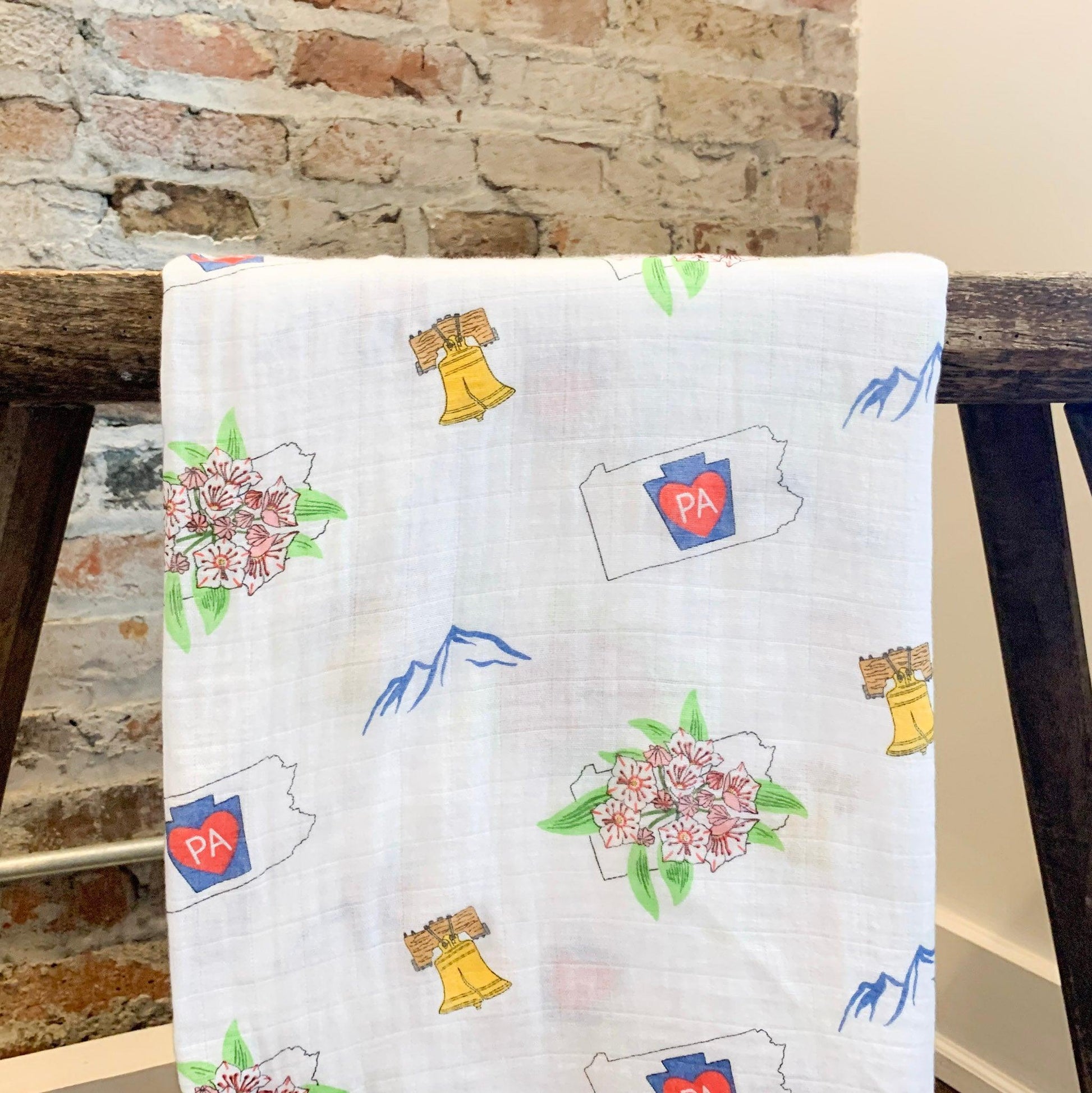 Pennsylvania-themed baby muslin swaddle blanket with state icons like Liberty Bell, covered bridges, and barns.