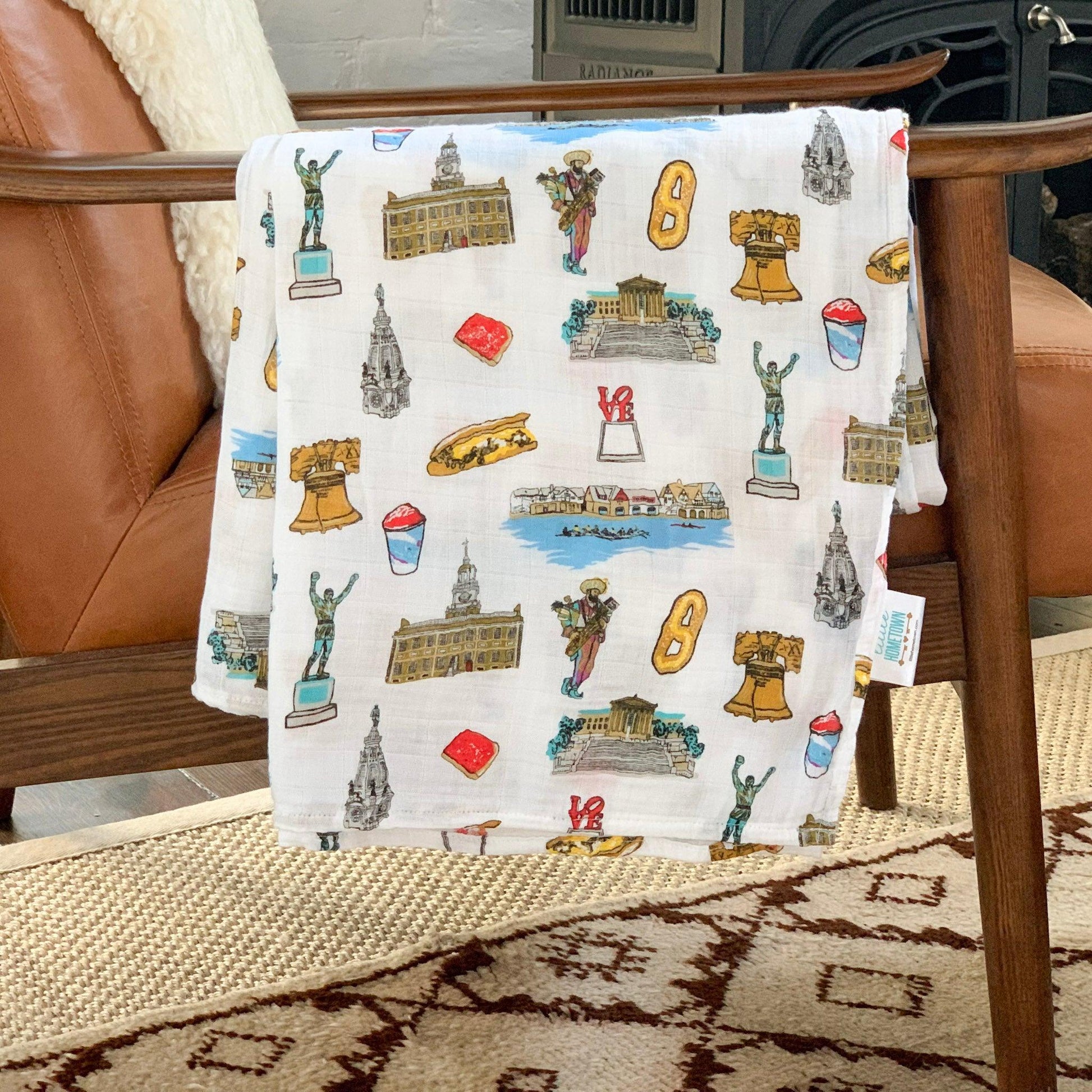 Philadelphia-themed baby muslin swaddle blanket with iconic landmarks in soft pastel colors on a white background.