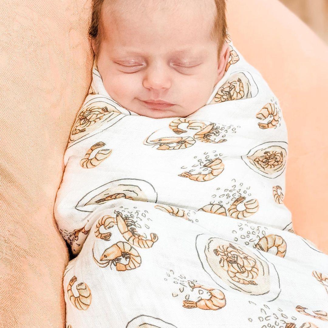 White muslin swaddle blanket with playful shrimp and grits pattern, featuring vibrant orange and yellow hues.