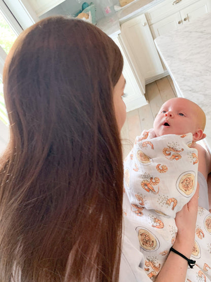 White muslin swaddle blanket with colorful shrimp and grits pattern, featuring bowls, shrimp, and corn.