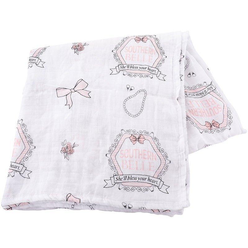 White muslin swaddle blanket with pink magnolia flowers and green leaves, folded neatly on a white background.