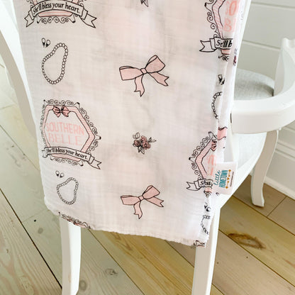 White muslin swaddle blanket with pink magnolia flowers and green leaves, folded neatly on a white background.