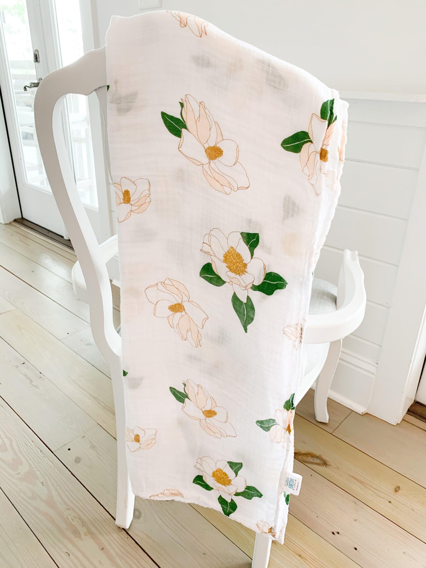 Soft muslin baby swaddle blanket with delicate Southern Magnolia floral print in pastel colors on a white background.