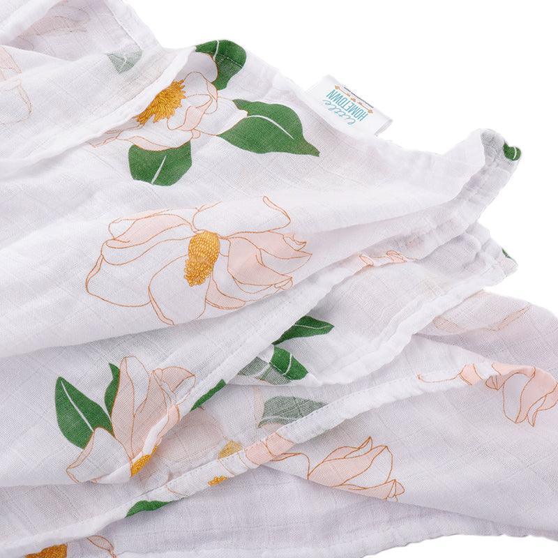 White muslin swaddle blanket with delicate Southern Magnolia floral print in soft pastel colors, neatly folded.