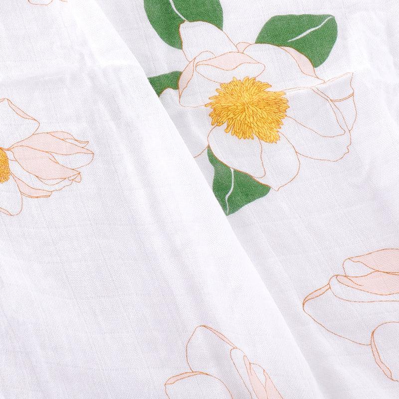 Soft muslin baby swaddle blanket with delicate Southern Magnolia floral print in pastel colors on a white background.