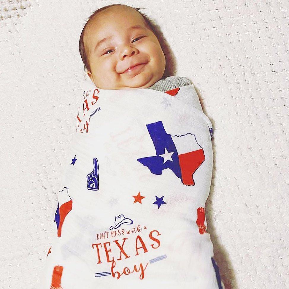 White muslin swaddle blanket with blue Texas-themed illustrations, including cowboy boots, hats, and state shapes.