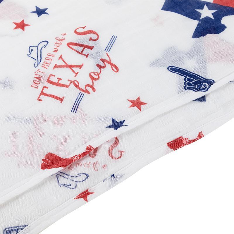 Baby boy swaddled in a white muslin blanket with blue Texas-themed icons, including stars, boots, and hats.