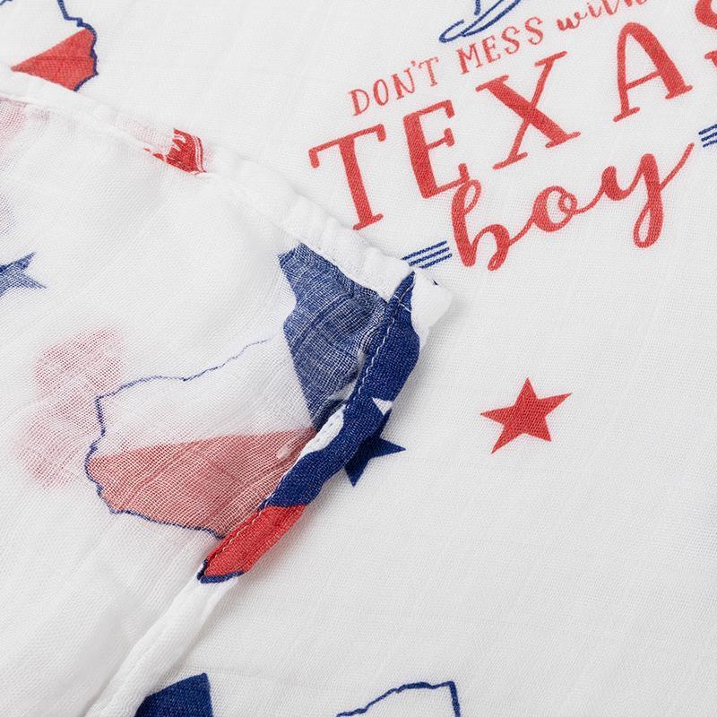 White muslin swaddle blanket with blue Texas-themed illustrations, including cowboy boots, hats, and state shapes.