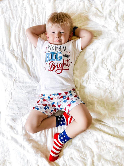 Child wearing Texas-themed pajamas with state icons, standing on a white background, smiling joyfully.