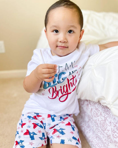 Child wearing Texas-themed pajamas with state icons, standing on a wooden floor, smiling joyfully.