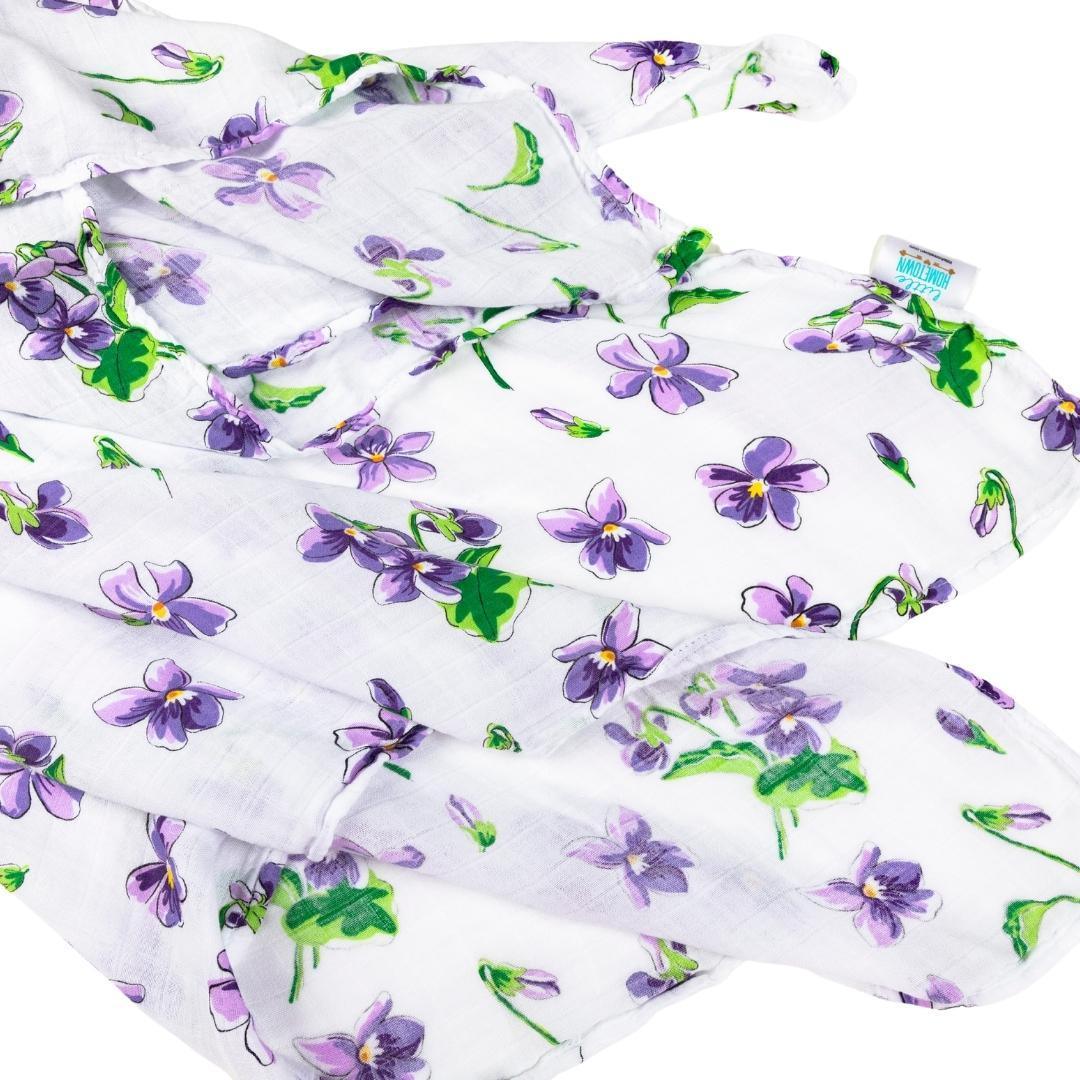 Soft violet muslin swaddle blanket with white floral patterns, neatly folded on a white background.