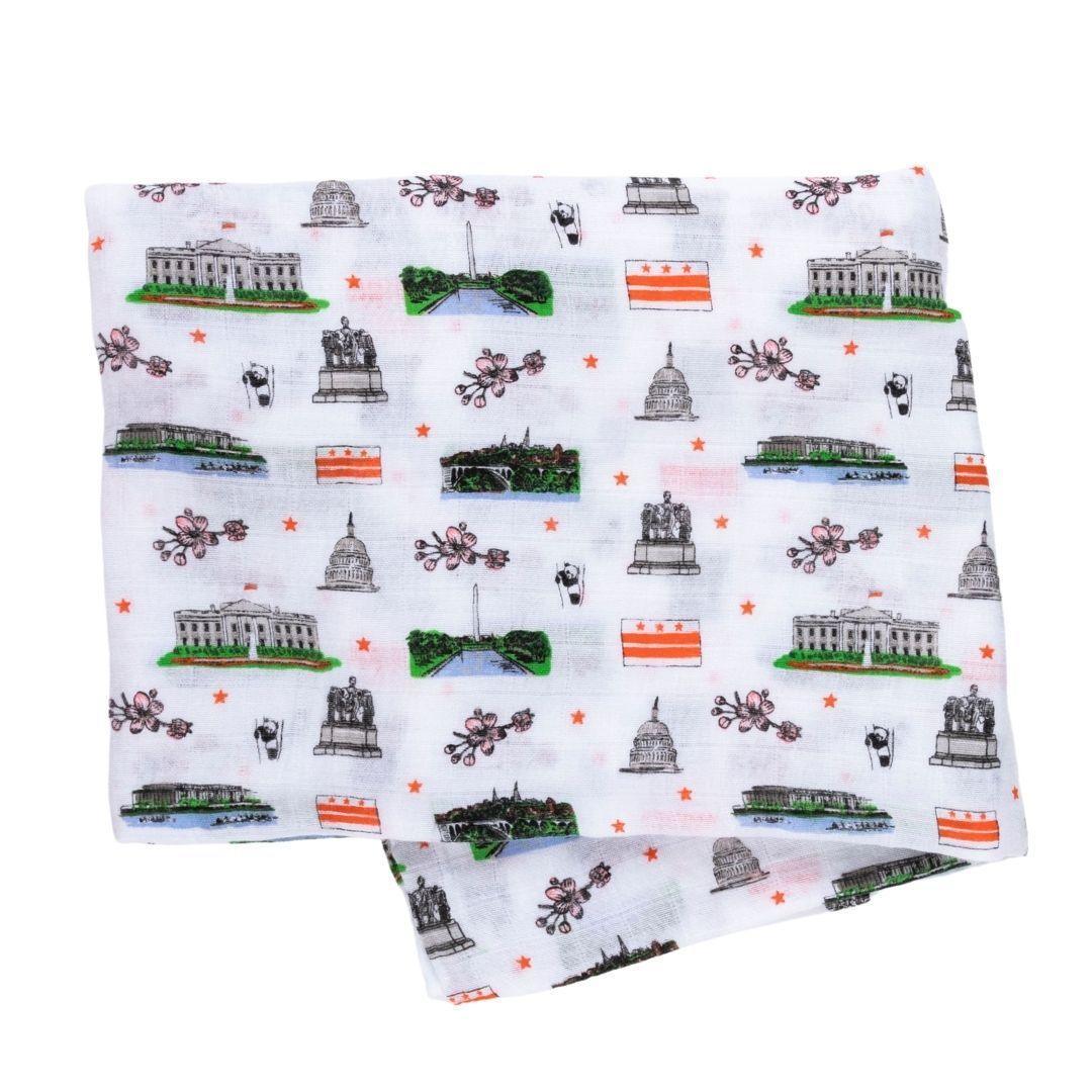 White muslin swaddle blanket with colorful illustrations of Washington D.C. landmarks, including the Capitol and Lincoln Memorial.